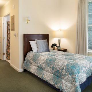 A cozy bedroom with a single bed adorned with a patterned quilt, accompanied by a nightstand and a wall-mounted lamp.
