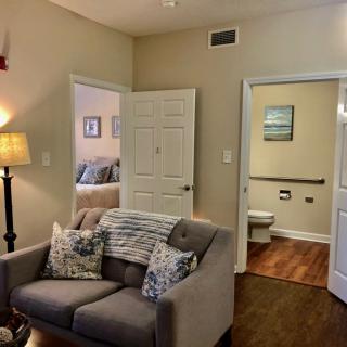 A cozy living room with a sofa and decorative cushions, leading to a bedroom and bathroom.