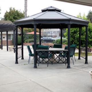 A metal gazebo with a table and chairs in a paved backyard area.
