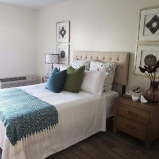 A cozy bedroom featuring a neatly made bed with decorative pillows and a textured blanket, accompanied by a stylish nightstand and wall art.
