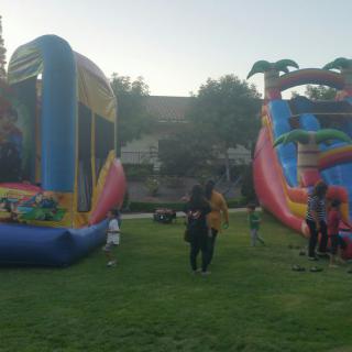 Children playing on an inflatable bounce house and slide at an outdoor event in a park.