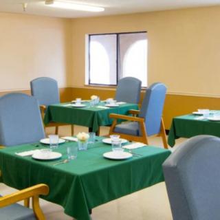 A dining room with several tables set for a meal, covered with green tablecloths and surrounded by blue chairs.