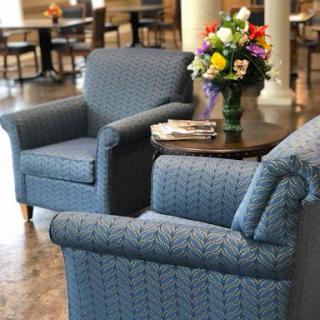 A cozy living area featuring two blue patterned chairs, a small table, and a vibrant bouquet of flowers.