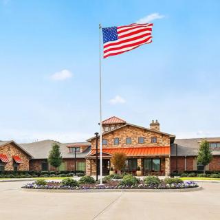 A large American flag waves in front of a building with well-maintained landscaping.