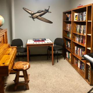 A cozy room featuring a piano, bookshelf filled with books, and a table set for games.