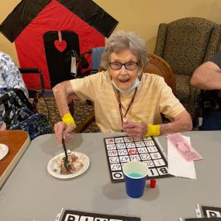 An elderly woman enjoying a game of bingo while having dessert at a community gathering.