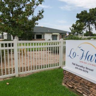 A fenced property with a building and a sign in front, surrounded by trees and grass.