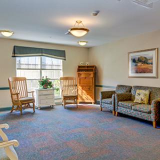 A cozy living room with rocking chairs and a sofa, featuring a large window and warm lighting.