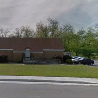 A small brick building with a parking lot and surrounding greenery.