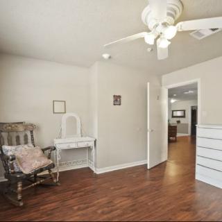 A cozy room with wooden flooring, featuring a rocking chair, vanity table, and ceiling fan.