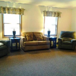 A cozy living room featuring a sofa, two chairs, side tables with lamps, and large windows.