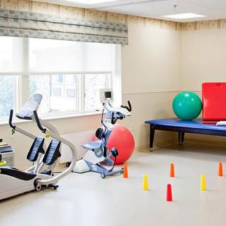 A bright and airy physical therapy room equipped with a stationary bike, exercise balls, and training cones.