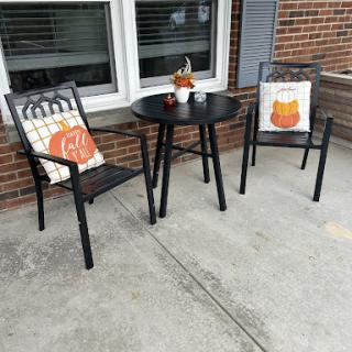A charming outdoor seating area decorated for autumn with a round table, two chairs adorned with pumpkin-themed cushions, and a small centerpiece.