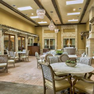 A spacious and elegantly decorated dining area with multiple tables and chairs, warm color tones, and decorative ceiling lights.