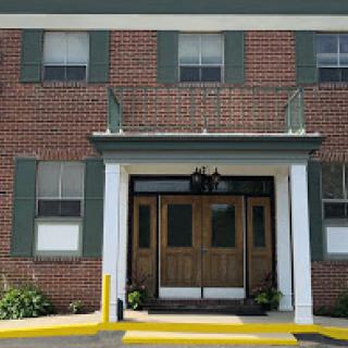 A brick building featuring a welcoming entrance with wooden doors and green shutters.