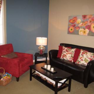 A cozy living room with a red armchair, black sofa with floral cushions, and a coffee table adorned with candles.