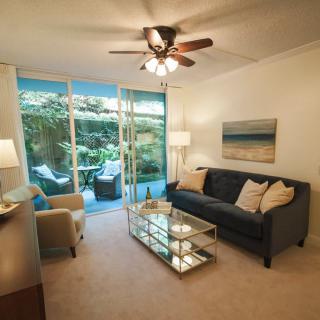 A cozy living room with a comfortable sofa, glass coffee table, and a view of the garden through sliding glass doors.