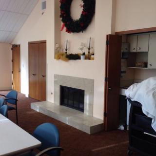 A cozy meeting room featuring a fireplace with a decorative wreath above it, surrounded by tables and chairs.