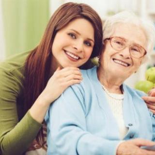 A young woman and an elderly woman smiling together indoors, showcasing a moment of togetherness and affection.