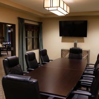 A modern conference room with a large meeting table and chairs, featuring a wall-mounted television.