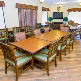 A dining area with wooden tables and chairs, featuring a television and wood flooring.