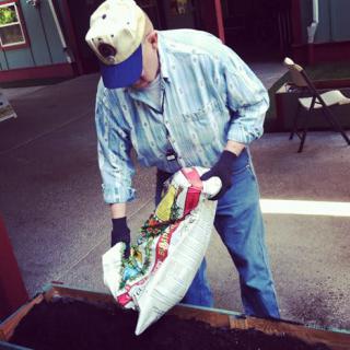 A person preparing soil by pouring it into a planter for gardening.