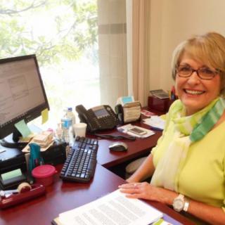 A woman sitting at her desk in an office, smiling at the camera.