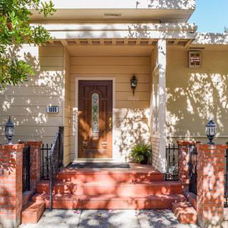 A quaint yellow house entrance with a wooden door and red brick steps adorned with outdoor lighting.