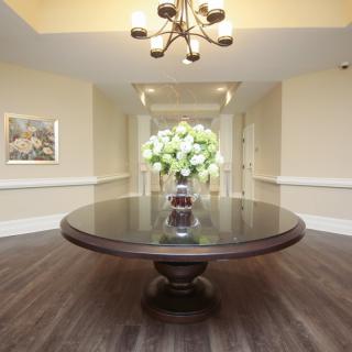 A hallway with a large round table decorated with a vase of flowers under an elegant chandelier.