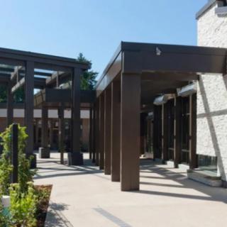 A modern building with large glass windows and a shaded outdoor area under clear blue skies.