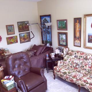 A cozy living room featuring a floral sofa, leather armchair, and various artworks on the walls.