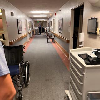 A healthcare worker navigating a hallway in a hospital, with medical equipment and wheelchairs visible.