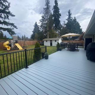 A spacious backyard featuring a wooden deck with outdoor furniture and an umbrella, alongside a children's playground set on a cloudy day.