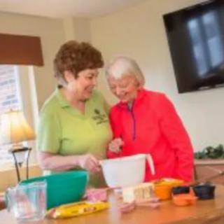 Two elderly women smiling while preparing food together in a kitchen.
