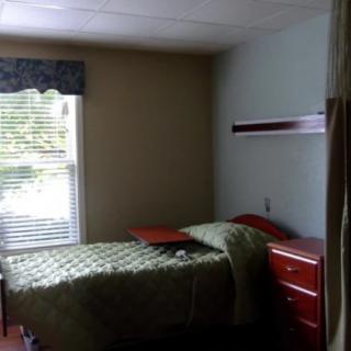 A minimalist bedroom with a single bed, dresser, and window with closed blinds.