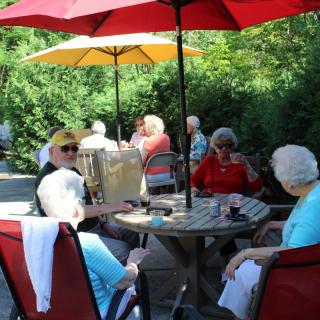 A group of seniors socializing on a sunny patio under colorful umbrellas.