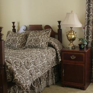 A cozy bedroom with patterned bedding and matching curtains, featuring a wooden bed frame and a nightstand with a lamp.