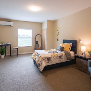 A cozy bedroom interior with a single bed, bedside table lamp, and window.