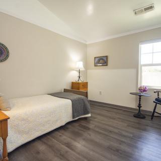 A minimalist bedroom with a single bed, lamp, and wooden flooring.