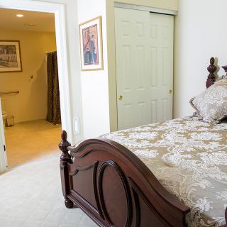 A cozy bedroom with a wooden bedframe and floral bedding, adjacent to an open bathroom door.