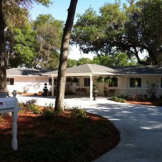 A charming single-story house with a curved driveway and surrounding trees.