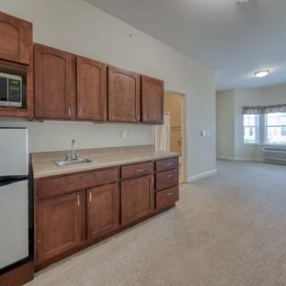 A modern apartment kitchen with wooden cabinets and a compact refrigerator.
