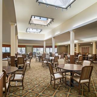 A spacious dining area with multiple tables and chairs, featuring elegant lighting and a carpeted floor.