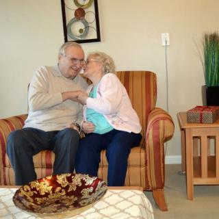 An elderly couple sharing a tender moment while seated in a cozy living room.