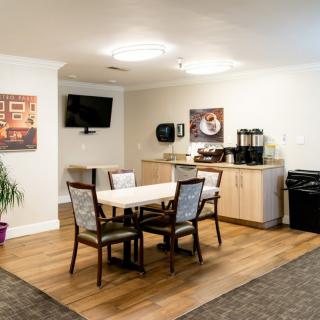 A cozy dining area with a table and chairs, featuring a coffee station and a television mounted on the wall.