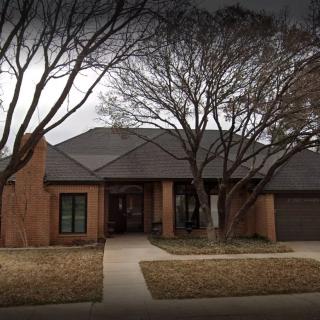 A suburban brick house with bare trees in the front yard.