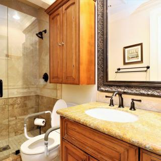 A well-lit bathroom featuring a wooden cabinet, a granite countertop sink, and a glass-enclosed shower.