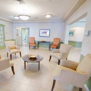 A spacious waiting area with comfortable chairs and a central table, illuminated by ceiling lights.