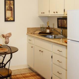 A cozy apartment kitchen with a small dining table and chairs, featuring cabinets, a sink, and a refrigerator.