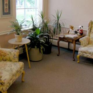 A cozy living room area with floral-patterned chairs, potted plants, and a small table by a window.